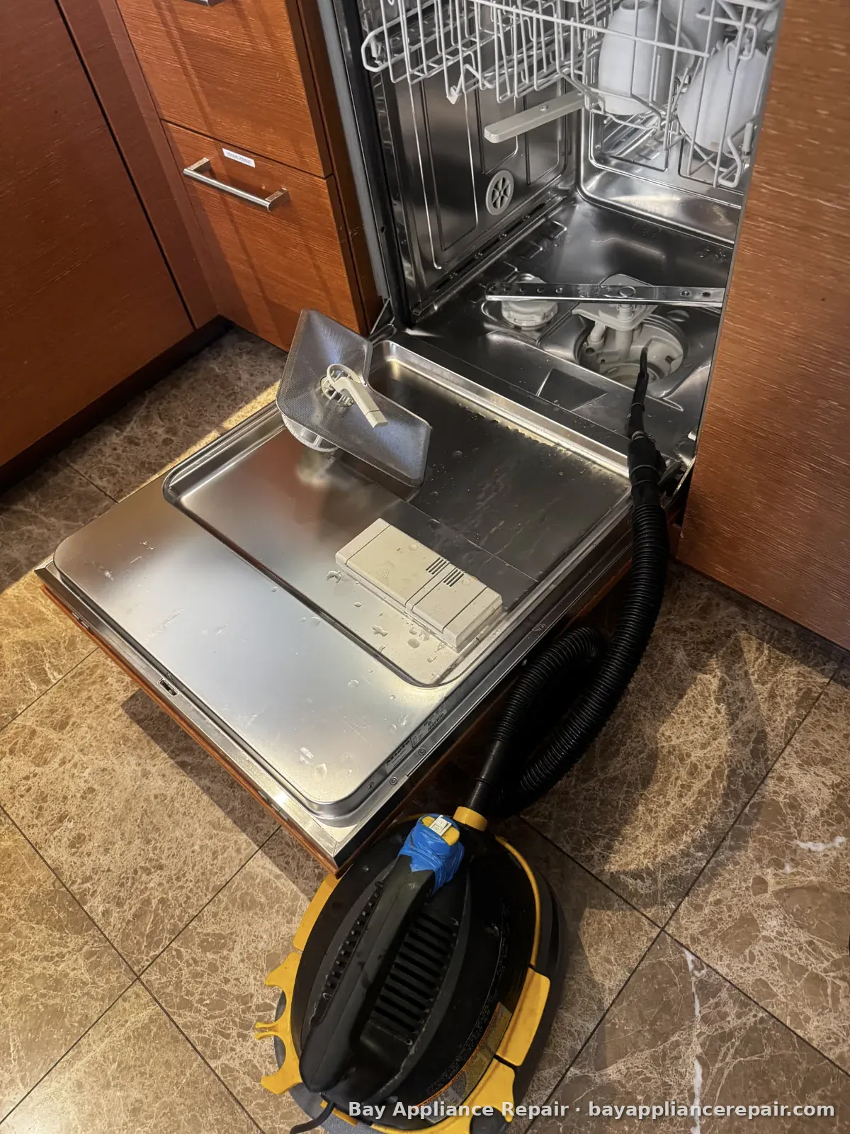 Dishwasher with the lower rack out and a shop vacuum hose draining water from the sump