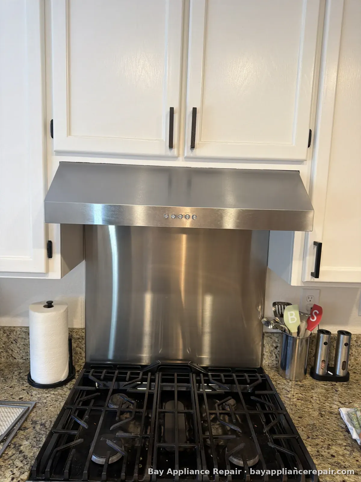 Gas cooktop under a stainless steel range hood and backsplash