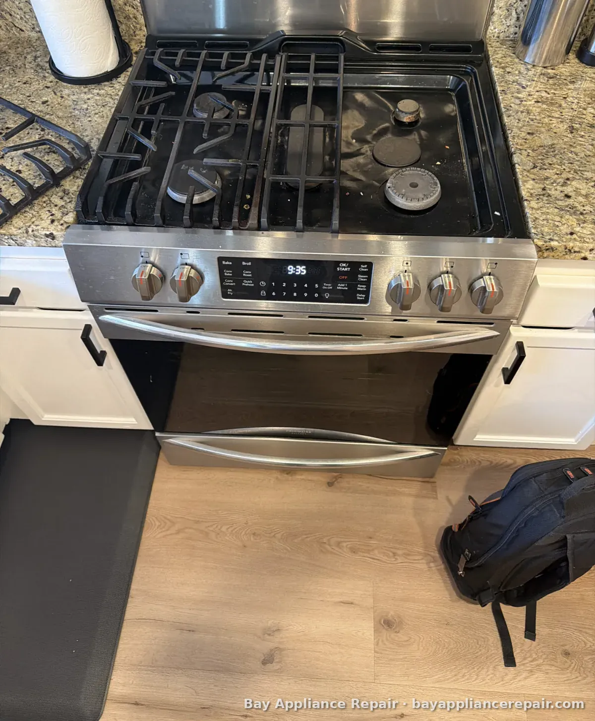 Freestanding stainless gas range during a repair, with a tool bag on the floor
