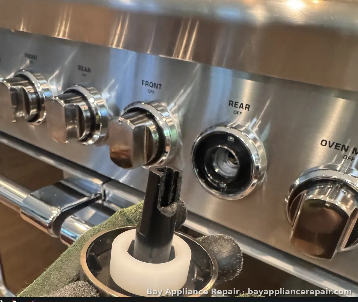 Range control panel with one burner knob removed, showing the valve stem